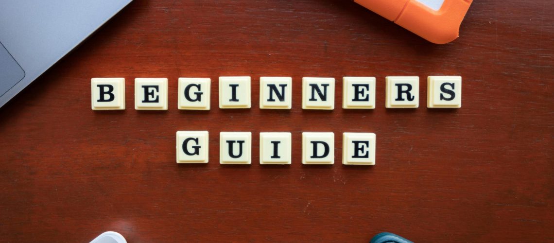 Creative flat lay of gadgets and 'Beginners Guide' text on wooden table.